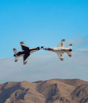 Two military planes flying closely past each other over desert mountains