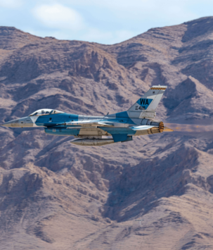 Military plane flying in front of a desert mountain range