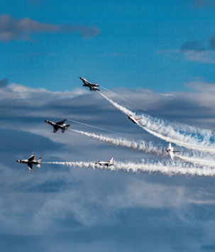 A group of military planes breaking out of formation against a blue sky