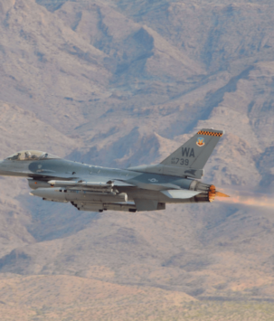 Military plane flying in front of a desert mountain landscape