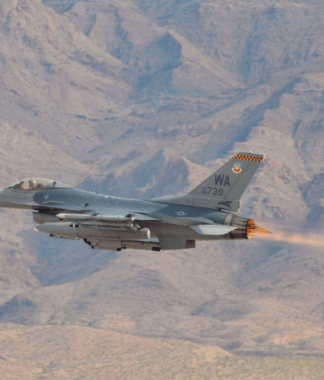Military plane flying in front of a desert mountain landscape