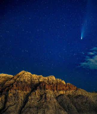 Stars in the night sky with a comet flying above a desert ridge
