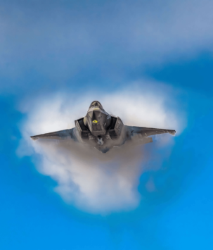 Frontal view of a military plane flying through a blue sky